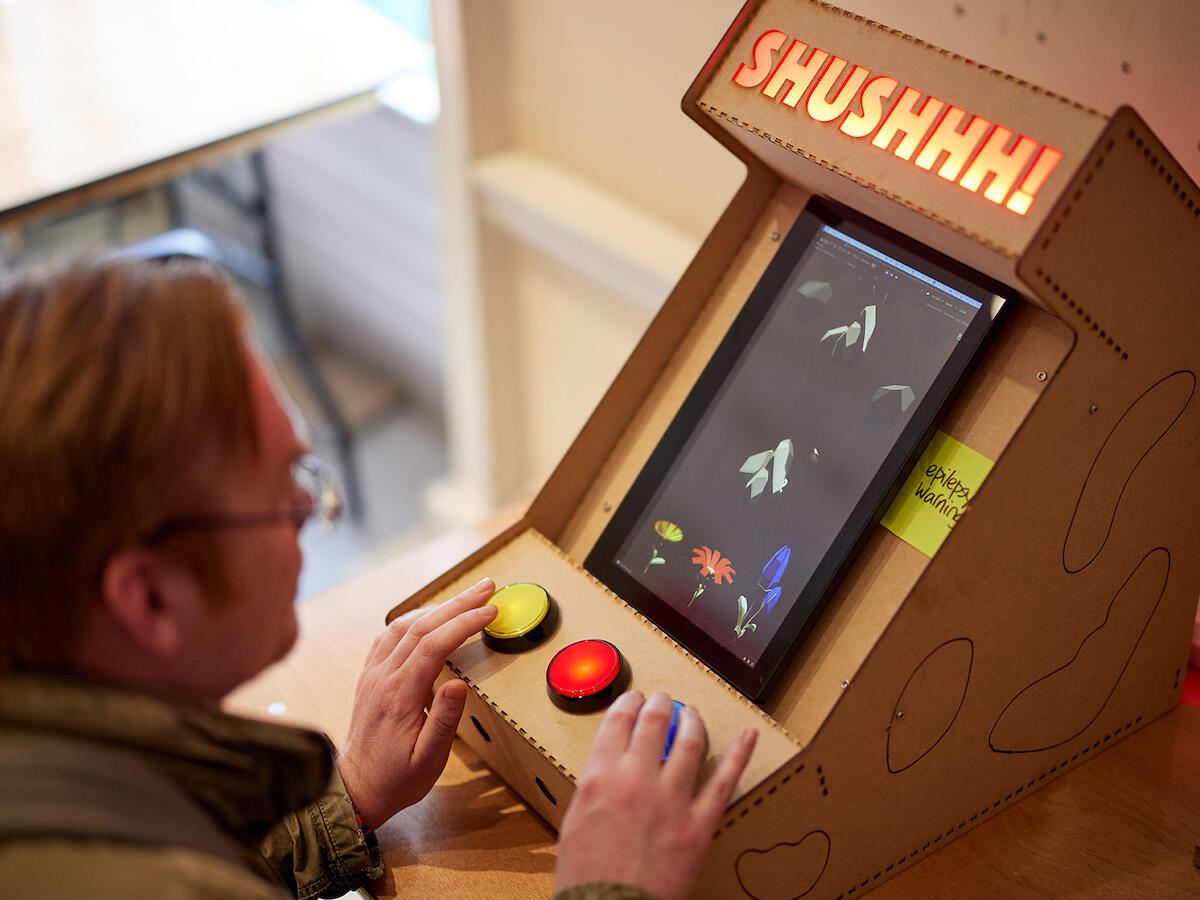 Man playing an arcade machine game called Shushhh! with yellow, red, blue buttons